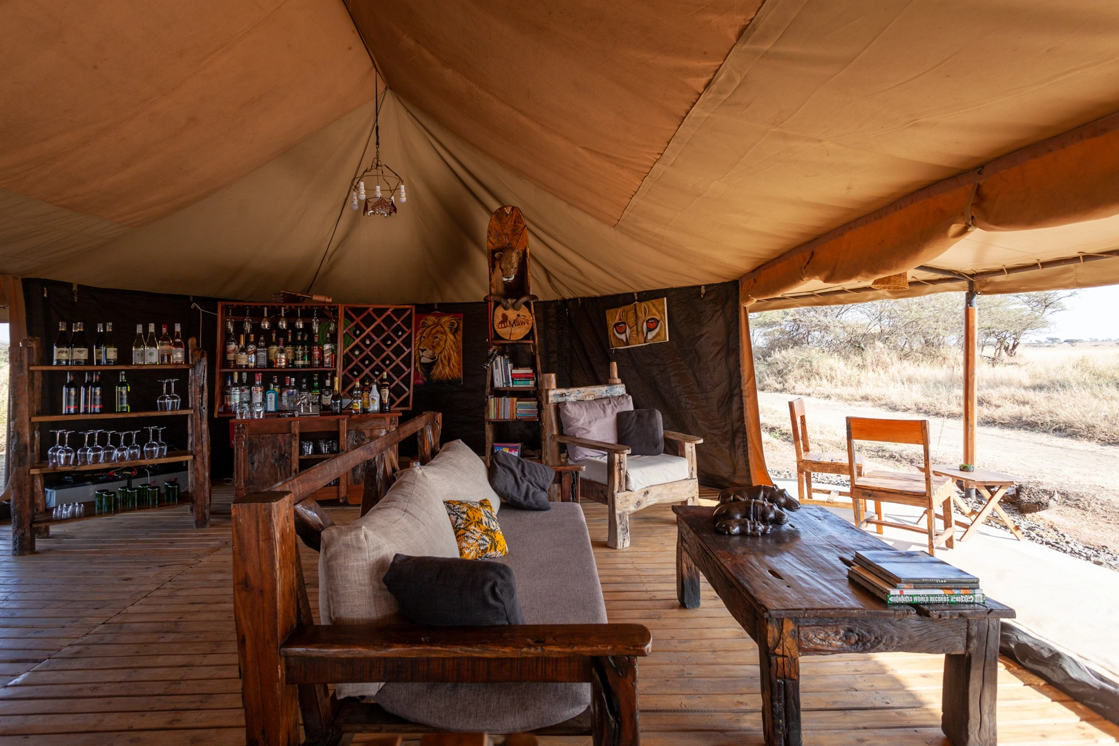 Salon Mawe Camp : tente de luxe avec mobilier en bois, bar, décor africain et vue sur la savane.