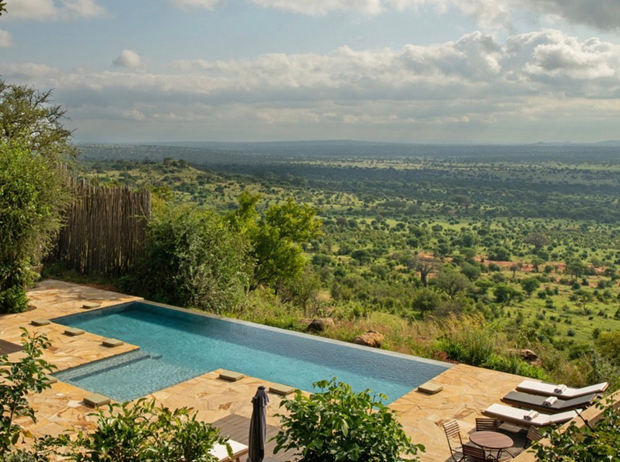 Infinity pool overlooking expansive green savannah under a cloudy sky