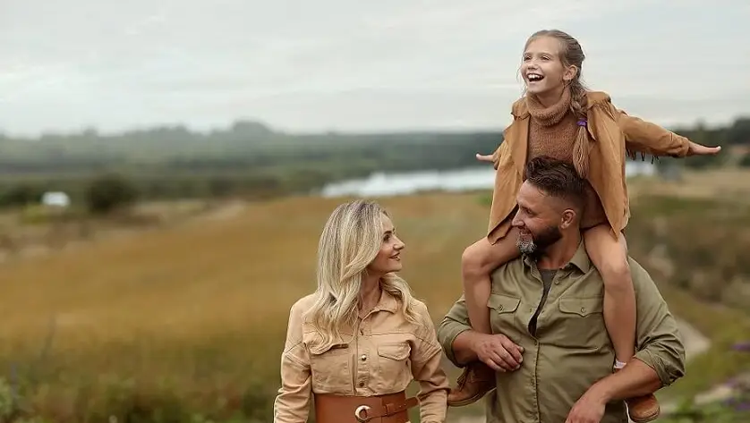 A family of three, a man, woman, and child, stands in a grassy field, exploring the joys of a safari experience.