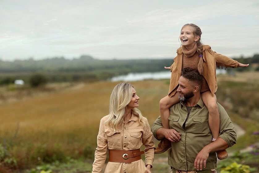 A family of three, a man, woman, and child, stands in a grassy field, exploring the joys of a safari experience.