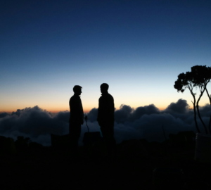 Our Tour Guide with Tourist against a twilight sky with clouds beneath on Umbwe Route