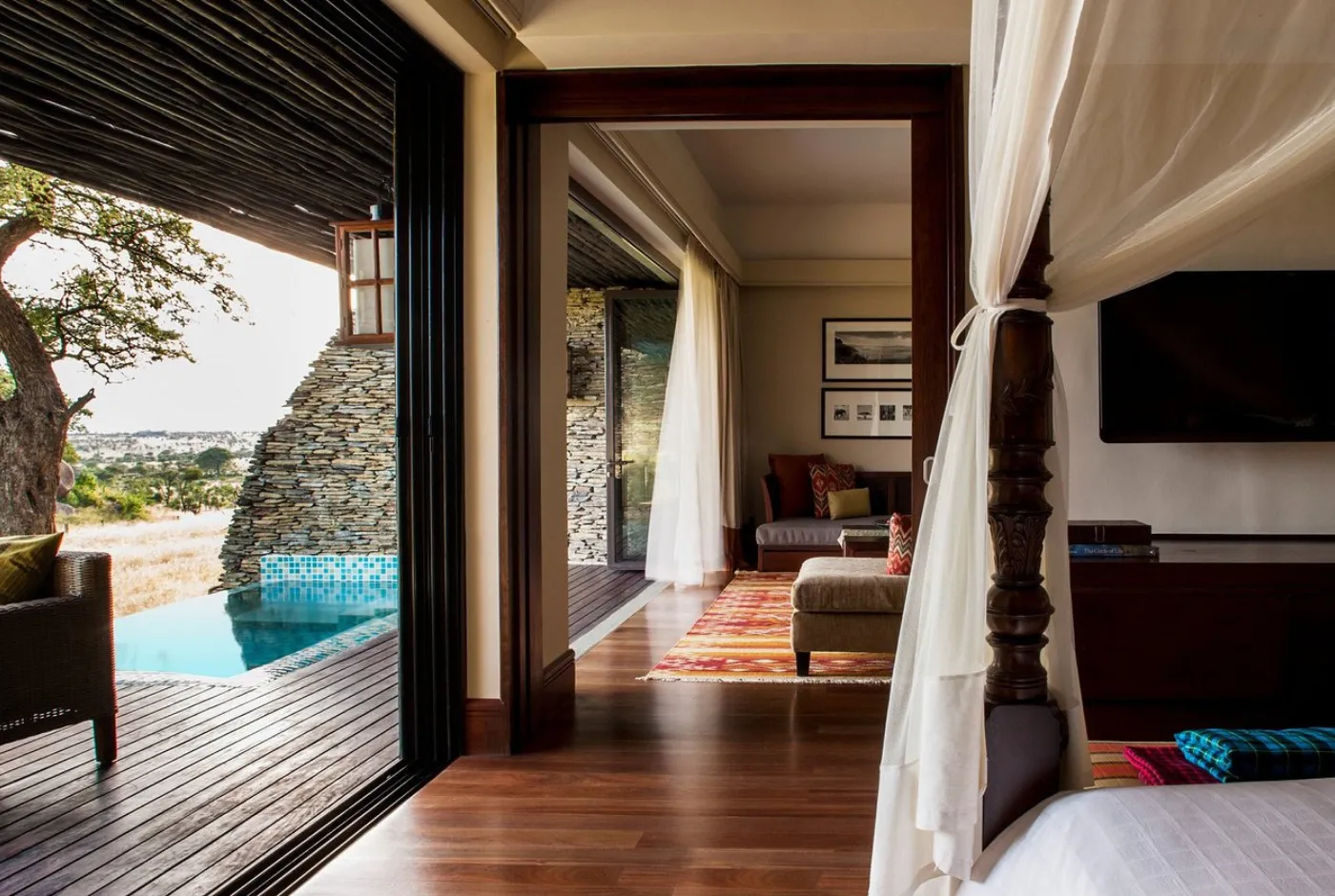 A suite with a canopy bed opening to a lounge and a private plunge pool on the deck
