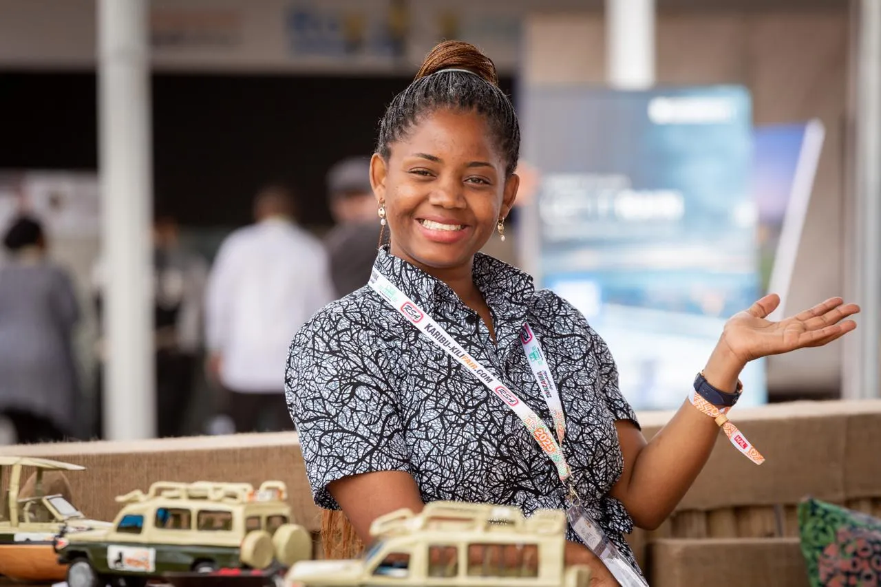 Un membre souriant de l’équipe Kilidove Tours sur un stand d’expo de voyage, avec des véhicules de safari miniatures