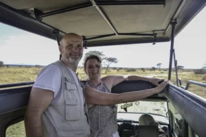 A smiling couple standing inside a pop-up roof 4x4 safari vehicle looking out over the open savannah, highlighting essential packing and safari prep tips for tanzania travel advice.
