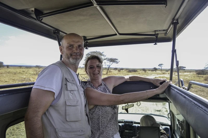 A smiling couple standing inside a pop-up roof 4x4 safari vehicle looking out over the open savannah, highlighting essential packing and safari prep tips for tanzania travel advice.