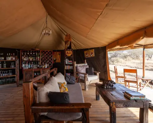 Lounge Mawe Camp: luxury tent with wooden furniture, a bar, African decor, and savannah views.