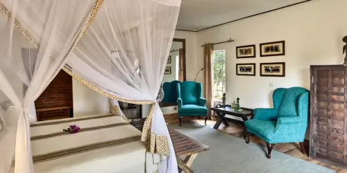 Cozy bedroom featuring a four-poster bed with delicate drapes, turquoise chairs, wooden accents, and artistic wall decor