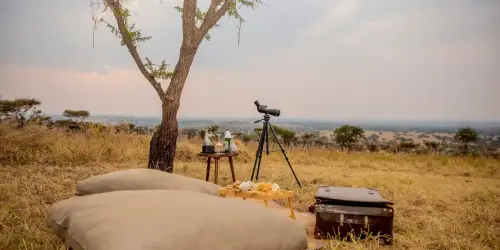 Outdoor relaxation setup with a telescope, drinks on a table, and snacks in Serenget Retreat Luxury Camp.