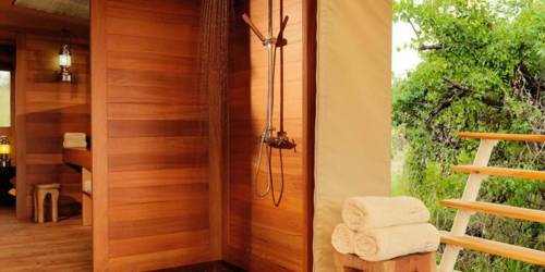 Outdoor wooden glamping bathroom with open shower, towels, and natural views