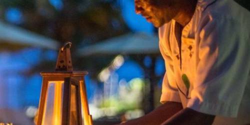 A waiter arranging a table by candlelight in a dimly lit outdoor setting