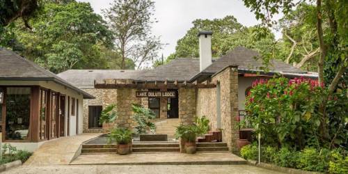 The Lake Duluti Lodge, a rustic stone and wooden building, surrounded by lush greenery and colorful flowers, welcomes visitors