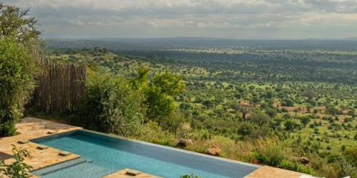 Infinity pool overlooking expansive green savannah under a cloudy sky