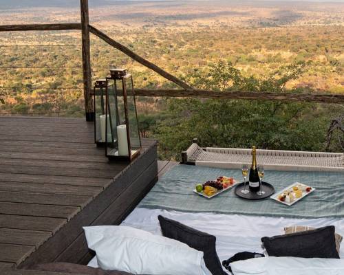 Outdoor lounge area with a bed overlooking a vast savannah landscape.