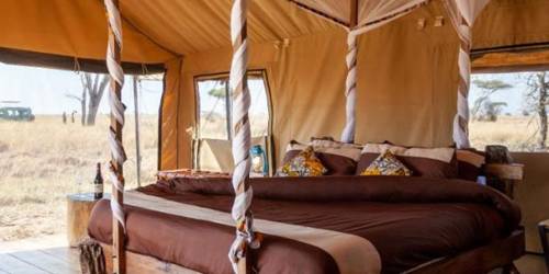 A rustic four-poster bed with white sheer drapes in a canvas tent room at Mawe Tented Camp