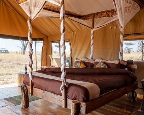 A rustic four-poster bed with white sheer drapes in a canvas tent room at Mawe Tented Camp