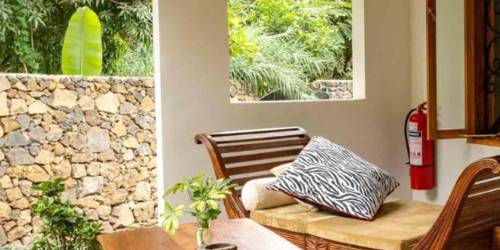 A cozy patio space with wicker furniture, plants, and an arched window view of greenery