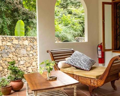A cozy patio space with wicker furniture, plants, and an arched window view of greenery