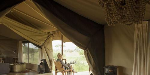 Luxurious tent interior with a woman relaxing on a wooden deck, featuring rustic decor and a chandelier made of beads