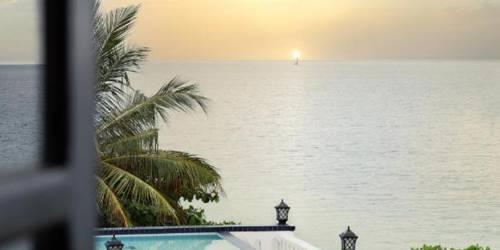 Sunset view over the ocean seen through an open window with a silhouette of palm trees and balcony